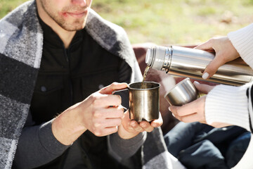 Homeless man with woman pouring hot tea in park, closeup