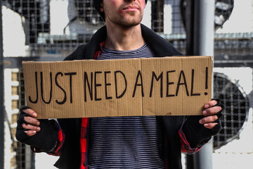 Homeless man holding cardboard with text JUST NEED A MEAL on street, closeup
