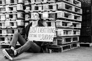 Homeless man holding cardboard with text LOST EVERYTHING TRYING TO SURVIVE on street
