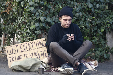 Homeless man and cardboard with text LOST EVERYTHING TRYING TO SURVIVE on street