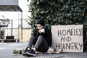 Homeless man with cardboard eating bread on street