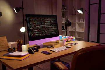 Programmer's desk with computer and glowing lamps in office at night