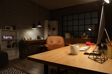 Interior of dark programmer's office with desks and glowing lamps at night