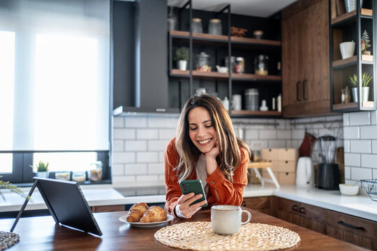 Happy woman using smartphone and enjoying breakfast in modern kitchen