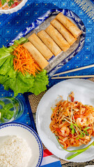 Crisp spring rolls serenade beside vibrant shrimp pad thai, evoking Songkran's zest and culinary...
