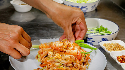 Sizzling shrimp pad thai garnished by Southeast Asian female hands, evoking Songkran celebration...