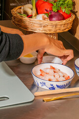 A delicate Asian hand prepares succulent shrimp, echoing Lunar New Year feasts and coastal mid-summer rituals, with vibrant produce nearby