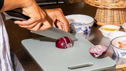 Cutting orb-like crimson onion, a culinary labyrinth on Harvest Moon Festival menu, Asian womans hands, rustic kitchen still-life