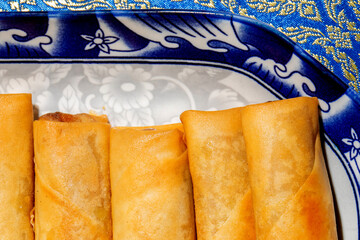 Crispy golden spring rolls rest on ornate porcelain, evoking Lunar New Year celebrations and savory...