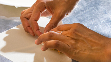 Crafting delicate origami, an East Asian woman's deft fingers conjure festive harmony, embodying...