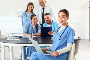 Female Asian medical intern working with laptop at table in clinic