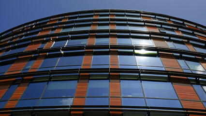 Modern glass and wood office building against blue sky. Curved facade features reflective windows and wooden panels. Contemporary urban architecture and innovative eco-friendly design aesthetics.