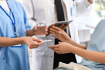 Medical intern giving pills and glass of water to patient in clinic, closeup