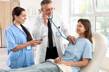 Female medical intern and doctor with stethoscope listening to patient in clinic