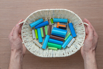 Top view, male hands holding a basket with batteries of different sizes for electrical appliances above the table.