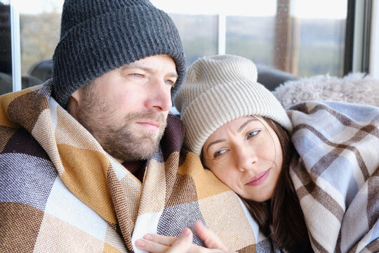 Couple relaxing on a patio wrapped on checkered blankets. Relaxed beautiful woman with a handsome man sitting on wooden cottage terrace. Winter resort. Happy loving couple enjoying leisure, embracing - Powered by Adobe