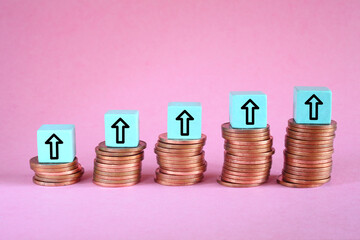 Business concept for financial growth, interest rate increase, inflation, high price, tax and tariffs rise . Arrow up sign on wooden cube blocks above stack of coins, free copy space
