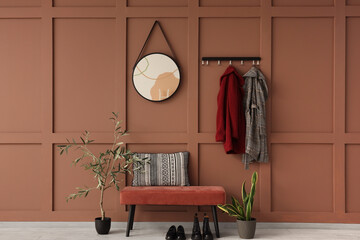 Interior of stylish hallway with pink bench, coats and mirror