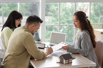 Female Asian real estate agent with couple signing agreement in office