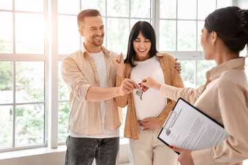 Real estate agent giving key from new house to pregnant couple in room