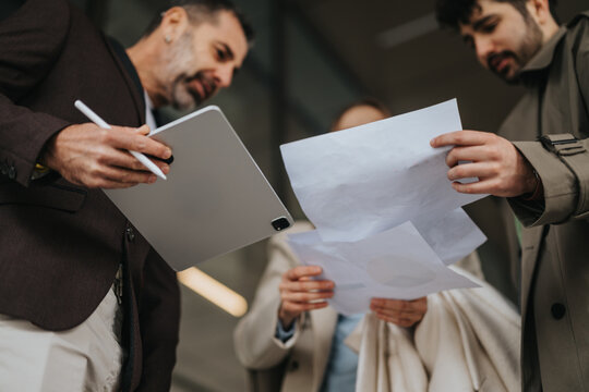 A team collaborates by reviewing printed documents and using a tablet stylus in an outdoor setting, reflecting teamwork, modern technology, and efficient communication.