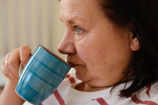 Senior woman having breakfast sitting in bed, drinking tea, enjoying her morning at home. Old lady eating from tray and using phone. Elderly female in pajamas relaxing with cup of coffee in a bedroom. - Powered by Adobe