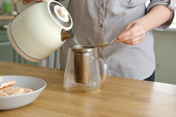Woman making tea. Female pouring a hot water to Glass teapot with black tea. Drinking hot tea, healthy freshly brewed detox drink. Preparing herbal tea in kitchen. Morning routine.