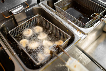 Close-up of mushrooms frying in hot oil in a commercial deep fryer, capturing the sizzling texture...