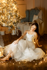 A girl in a white dress sits on the floor, surrounded by garlands against the backdrop of a shining...