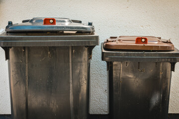 Trash bins stand ready for waste collection on a sunny day in an urban neighborhood, highlighting...