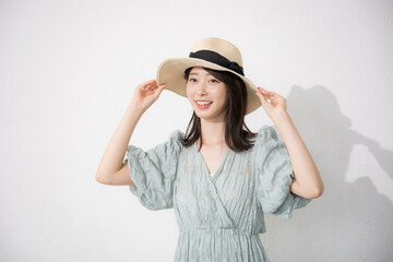 麦わら帽子を被って眩しい日焼けを気にする夏服の女性　白背景
