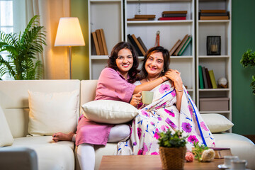 Indian old mother hugging daughter while chatting and holding hands in cozy modern home interior