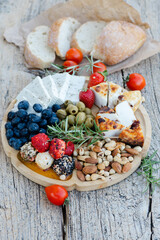 Wooden tray with delicious variety of cheese, nuts, olives, blueberries and strawberries, enjoying...