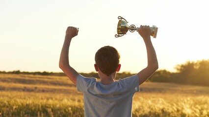 boy enjoys the open space of nature, raising trophy under warm sunlight. child feels free, joyful,...