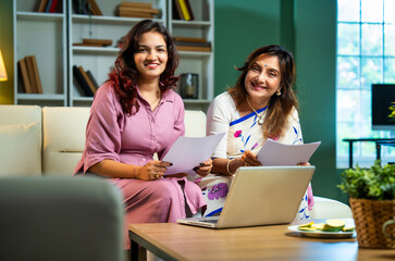 Indian mother daughter using laptop and documents together to manage home accounts and expenses