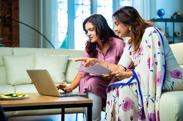 Indian mother daughter using laptop and documents together to manage home accounts and expenses