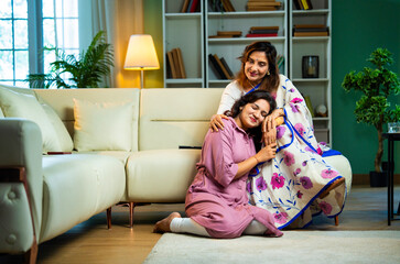 Indian old mother hugging daughter while chatting and holding hands in cozy modern home interior