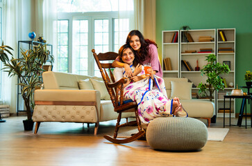 Indian woman serving orange juice to old mother in saree sitting on rocking chair at home