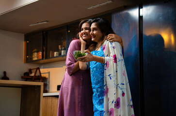 Daughter hugs mother after tasting delicious healthy green salad in modern Indian kitchen