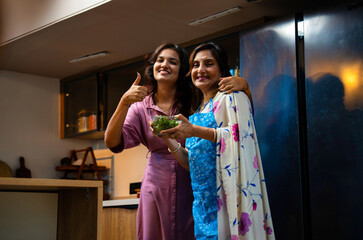 Daughter hugs mother after tasting delicious healthy green salad in modern Indian kitchen