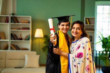 Indian Female graduate in gown shows degree to mother and hugs happily during home celebration