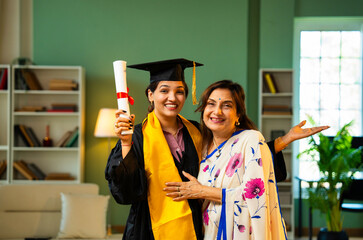 Indian Female graduate in gown shows degree to mother and hugs happily during home celebration
