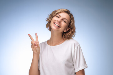 Joyful Young Woman Making Peace Sign with Smile on Light Blue Background