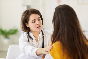 Compassionate female doctor in white coat sitting in bright medical office and gently comforting...