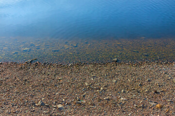 Small gravel stones on the shore near calm blue water