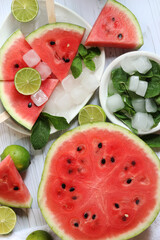 Ripe watermelon pieces on sticks like ice cream. Watermelon, lime and mint. Summer fruits background. Flat lay. Watermelon slices in white plate top view, wooden table and lime halves. Summer food