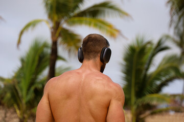 Muscular man in headphones on tropical sea beach on palm trees background