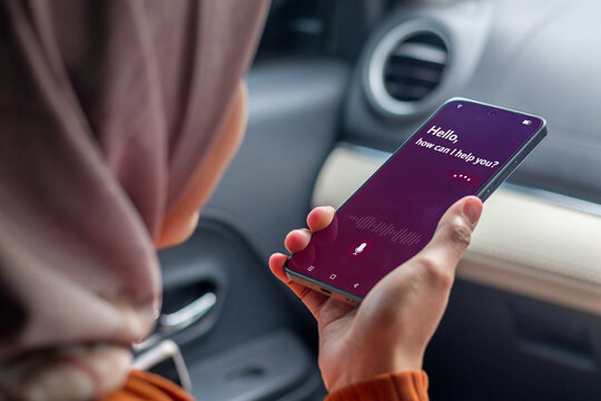 A Muslim woman in a car holding a smartphone to use virtual voice assistant