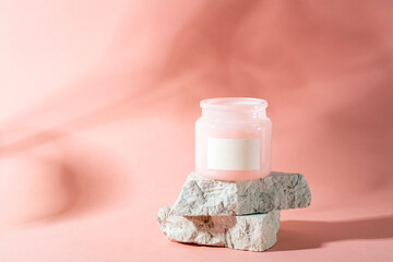 Cosmetic jar with blank label on stone podium over pastel pink background with light and shadows. Mockup