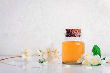 Glass bottle of essential oil with cork lid and jasmine flowers on white background. Copy space